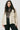 Woman wearing a beige trench coat over a gray sweater and black pants on a white background