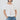 A model wearing a white short-sleeve blouse with voluminous puff sleeves and a smocked neckline, paired with light-wash blue jeans, against a plain light gray background.