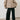 Person wearing a beige jacket and black pants against a plain background