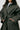 Person wearing a green trench coat with a white shirt underneath on a plain background