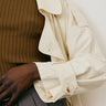 Close-up of a person wearing a butter trench coat with a blurred background