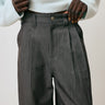Person wearing gray pleated pants and a light-colored sweater against a neutral background