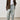 Person wearing a brown coat, white shirt, light blue jeans, and dark shoes on a plain background