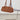 A brown suede duffle bag with dual top handles, hanging from a clear acrylic chair with a purple cushion on a metal cantilever chair in a minimalist room.