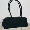 A black fabric duffel-style handbag with two long shoulder straps, displayed hanging from a clear stand in a minimalist indoor setting.